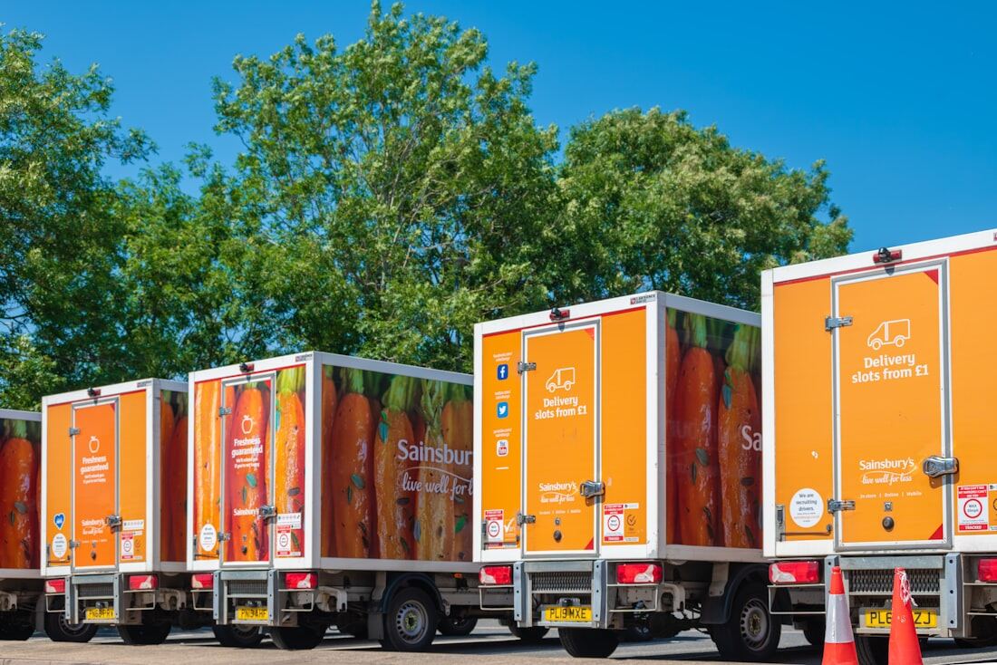 A row of orange delivery box trucks lined up in a depot.