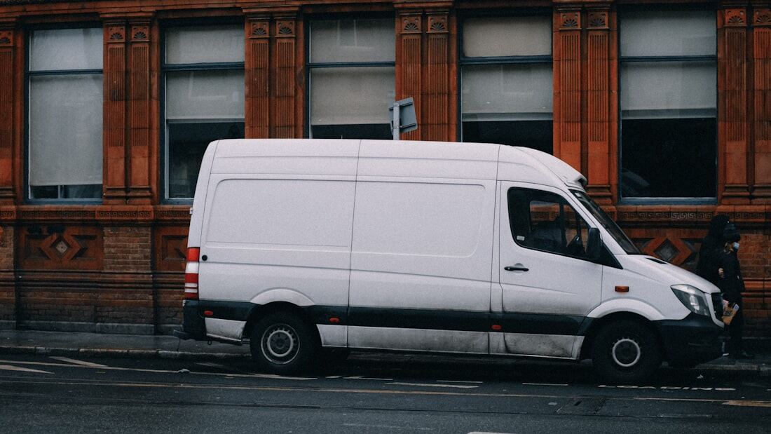 A clean white cargo van parked on a wet street.