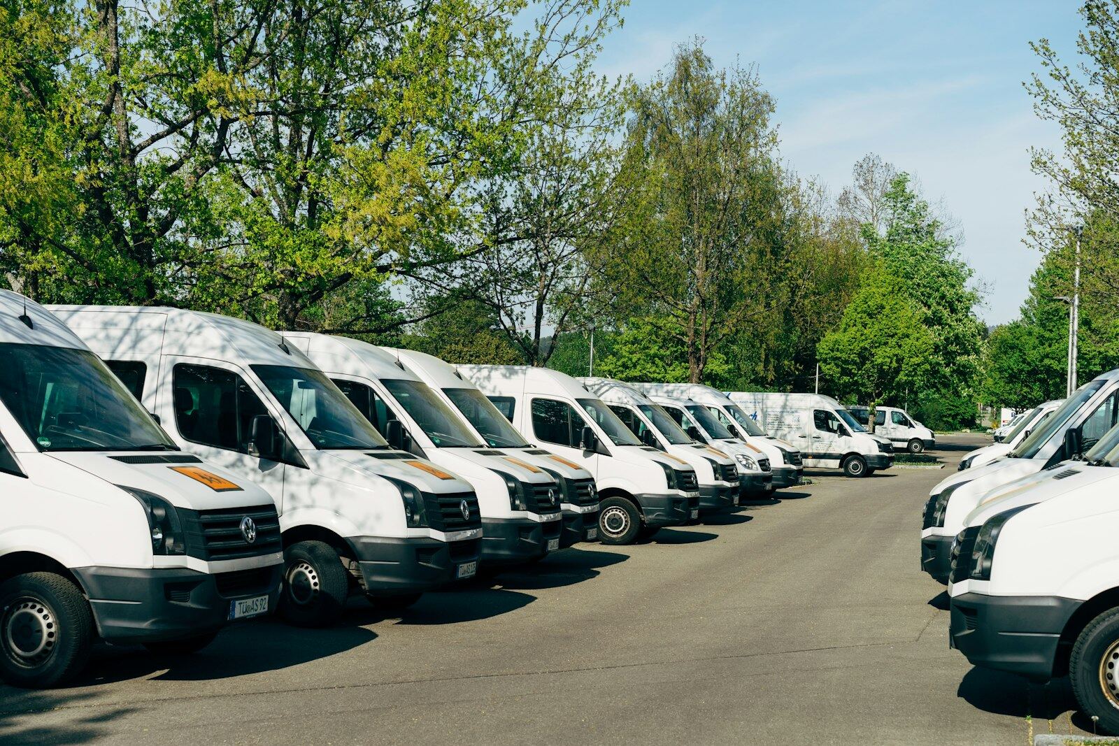 A long row of white cargo vans parked side by side in a company lot.