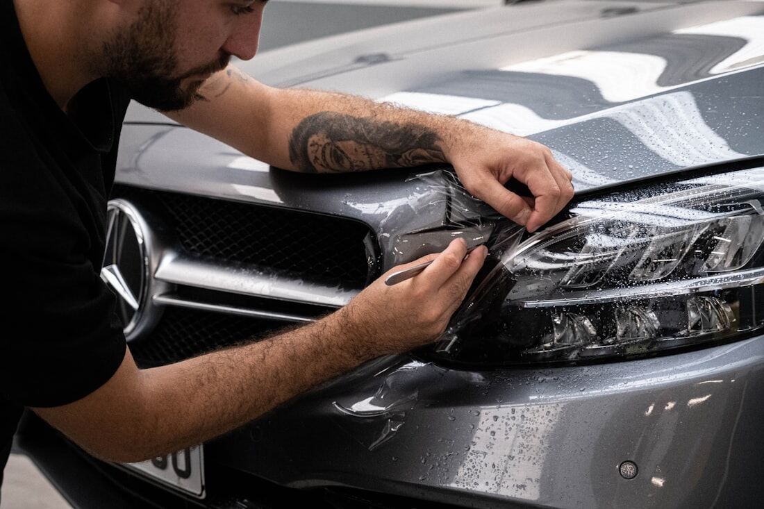 A detailer working along the headlight and front trim of a dark car.